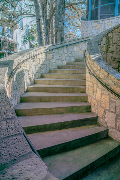 Betontreppen mit Steinwänden und montierten Handläufen in San Antonio, Texas. Treppen mit Betonstufen in der Nähe der blattlosen Bäume im Hintergrund. - Foto, Bild