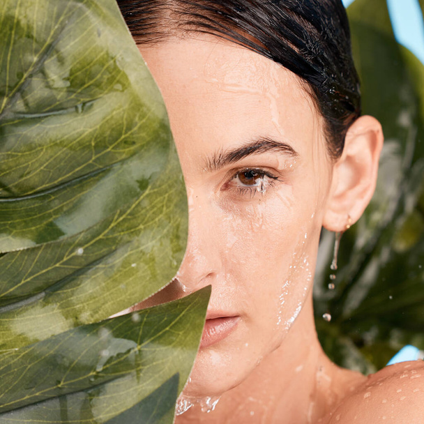 Monstera, skincare and woman in studio shower for natural makeup, beauty and eco friendly cosmetics with face aesthetic. Plant, leaf and nature with young model portrait and water drops for facial. - Fotó, kép