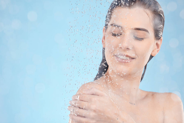 Shower, cleaning and woman with water in studio for spa wellness, body care and self care on blue background. Bathroom, skincare and water drops on girl washing body for hygiene, hydration and health. - Foto, Imagem