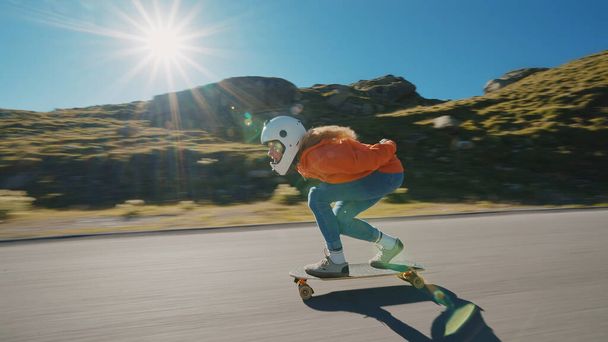 Cinematic downhill longboard session. Young woman skateboarding and making tricks between the curves on a mountain pass. Concept about extreme sports and people - 写真・画像