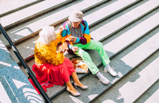 Παλιά μοντέρνο ζευγάρι ντύσιμο μοντέρνα χρωματιστά ρούχα. Νεανική γιαγιά και παππούς διασκεδάζουν έξω και τρελαίνονται. Εκπροσώπηση ηλικιωμένων ατόμων που αισθάνονται νέοι στο εσωτερικό - Φωτογραφία, εικόνα