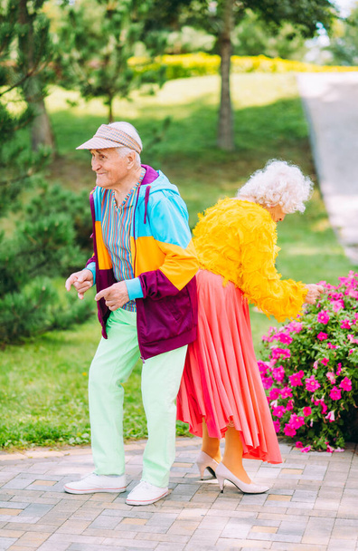 Old modern couple dressing fashionable colored clothes. Youthful grandmother and grandfather having fun outdoor and going wild. Representation of elderly people feeling young inside - Foto, Bild