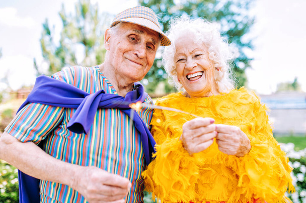 Old modern couple dressing fashionable colored clothes. Youthful grandmother and grandfather having fun outdoor and going wild. Representation of elderly people feeling young inside - 写真・画像