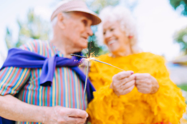 Old modern couple dressing fashionable colored clothes. Youthful grandmother and grandfather having fun outdoor and going wild. Representation of elderly people feeling young inside - Foto, afbeelding