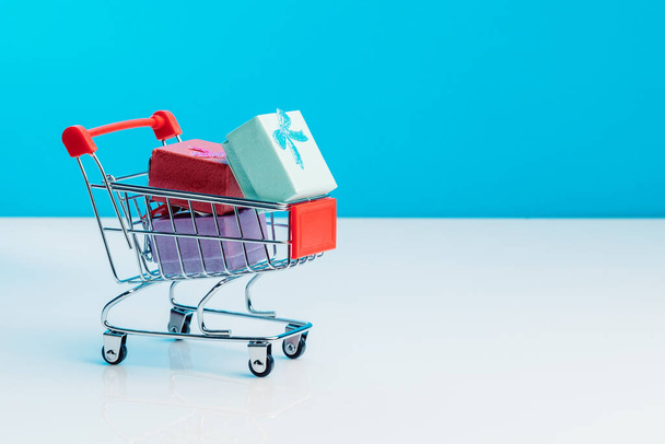 Shopping cart filled with presents isolated on blue background. Christmas, birthday and sale concept - Fotoğraf, Görsel