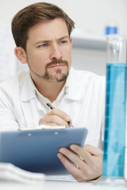 scientist looking at test tube and writing on the clipboard - Photo, image