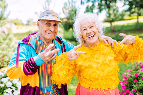Old modern couple dressing fashionable colored clothes. Youthful grandmother and grandfather having fun outdoor and going wild. Representation of elderly people feeling young inside - 写真・画像