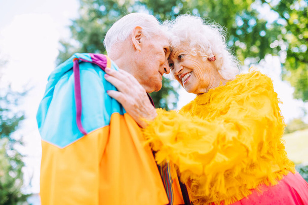 Old modern couple dressing fashionable colored clothes. Youthful grandmother and grandfather having fun outdoor and going wild. Representation of elderly people feeling young inside - Foto, imagen