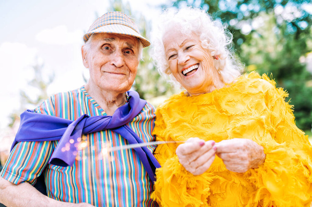 Старая современная пара одевается модной цветной одеждой. Молодые бабушка и дедушка веселятся на открытом воздухе и сходят с ума. Представление пожилых людей, чувствующих себя молодыми внутри - Фото, изображение