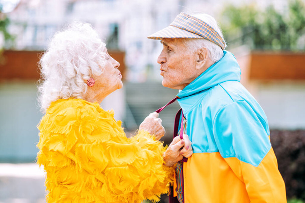 Old modern couple dressing fashionable colored clothes. Youthful grandmother and grandfather having fun outdoor and going wild. Representation of elderly people feeling young inside - Foto, imagen
