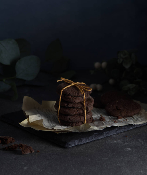 Chocolate chip cookies stacked and tied with string stand on shabby pages lying on a black stone - Foto, immagini