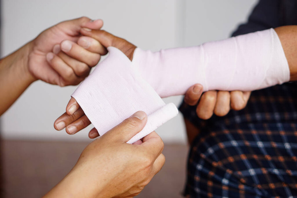 Die Hände des Close-ups umhüllen das verstauchte Handgelenk des Patienten mit einem elastischen Verband. Konzept, Erste Hilfe und Behandlung von Armverletzungen. Unfall. Versicherungen. - Foto, Bild