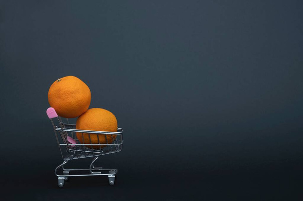 Les oranges mûres se trouvent dans un petit panier en métal dans les supermarchés - isolez-vous sur un fond de bannière noire dans un studio photo. Gros plan sur les fruits. - Photo, image