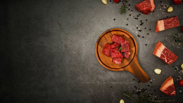 Raw picanha or rump beef meat chopped in cubes with pepper, sea salt and rosemary on black stone background. - Foto, Bild