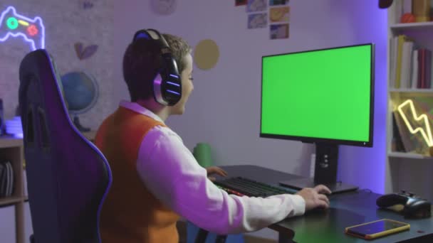 Стриминг и онлайн видеоигра на компьютере с наушниками и микрофоном, вид сзади. Зеленый экран, макет, пространство для копирования. Уютная комната светится теплым и неоновым светом. Высокое качество - Кадры, видео