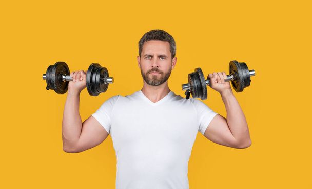 fit muscular fitness guy with barbell. muscular fitness guy training with barbell isolated on yellow. muscular fitness guy training with barbell in studio. muscular fitness guy hold barbell in shirt. - Fotó, kép