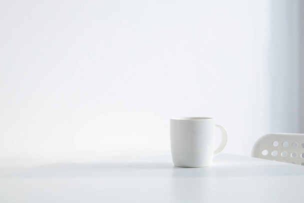 Weiße Tasse mit Kaffee auf weißem Tisch unter natürlichem Licht - Foto, Bild