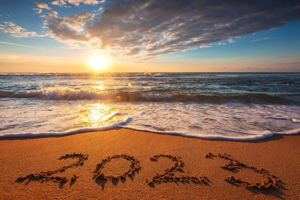 A szabadság, a motiváció, a pihenés, a boldogság és az életmód fogalma. Új év 2023 szöveges felirat a strandon homok napkeltekor. Trópusi óceáni reggel. - Fotó, kép