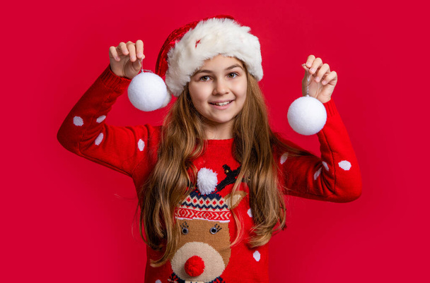 merry xmas. happy teen girl in santa hat with snowball on red xmas background. xmas teen girl in santa hat hold snowball. teen girl wear sweater hold xmas snowball. - Foto, Imagem