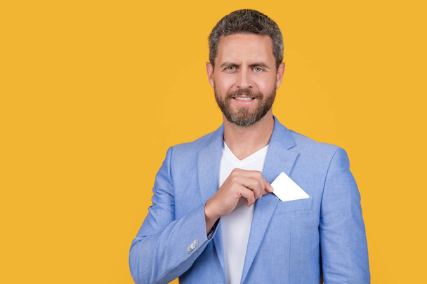 positive man with business credit card with copy space. man holding business credit card in studio. man in jacket hold business credit card. man hold business credit card isolated on yellow. - Foto, immagini