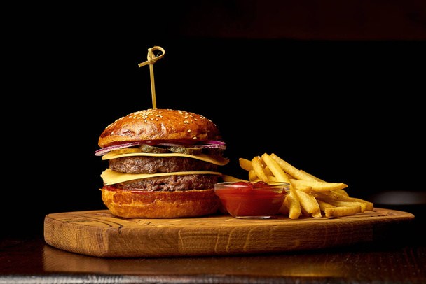 American fast food: double cheeseburger on a wooden board. Dark wooden background. Selective focus. Food for the pub - Photo, Image
