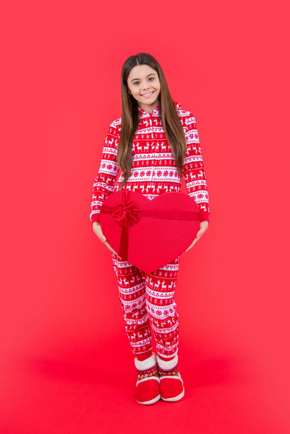 new year. positive teen girl with red new year present in studio. teen girl hold new year present standing isolated on red background. - Foto, Imagem