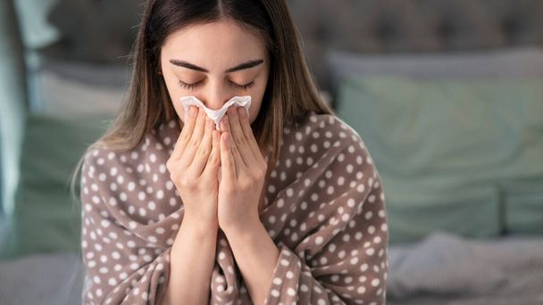jonge zieke vrouw blazen haar neus in bed - Foto, afbeelding