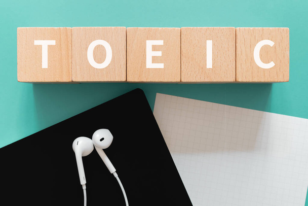 TOEIC listening; Five wooden blocks with TOEIC text of concept, a black notebook, a piece of paper, and a pair of earphones. - Foto, Bild