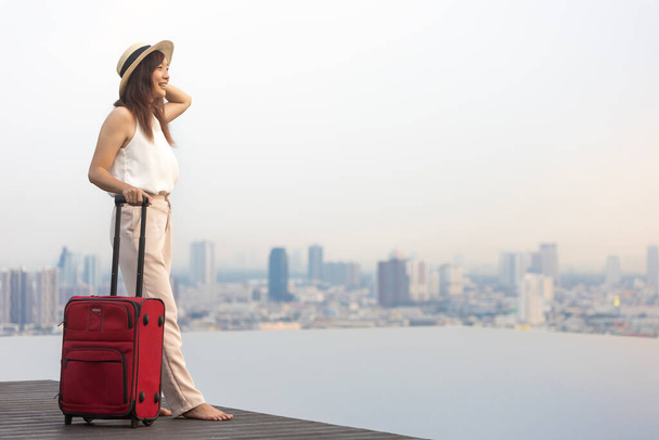Azji kobieta turysta z jej bagażu torba korzystających jej basen na dachu widok z tłem krajobraz miasta na wakacje i podróże - Zdjęcie, obraz