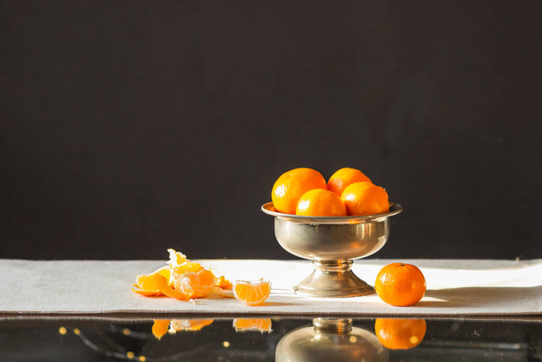 Still life with orange tangerine fruits in a vintage metal vase isolated on table with black background. Traditional sweet food for winter holidays. Preparation to New Year or Christmas eve. - Photo, Image