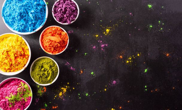 Top view of colorful holi powder with multicolored holi paint on dark background. Happy holi festival decoration concept. - Foto, immagini