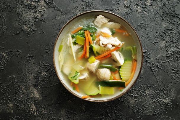 Тайский суп со стеклянной лапшой, овощами и курицей в керамической миске на темном фоне с копировальным пространством - Фото, изображение