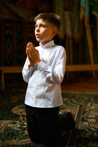 Ein Junge kniet im Gebet zu Gott, Kindergebet in der Kirche. - Foto, Bild
