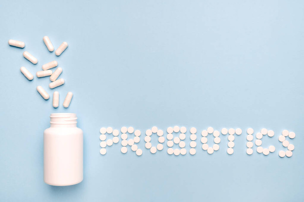Guts protection. Probiotics word made of pills, medicaments pills spilled from a white bottle. On blue background.  - Фото, изображение