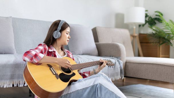 Woman practicing or learning to play guitar and practice using his fingers to hold guitar chords while looking at music notes with intention, Taking advantage of free time, Relax during free time. - 写真・画像