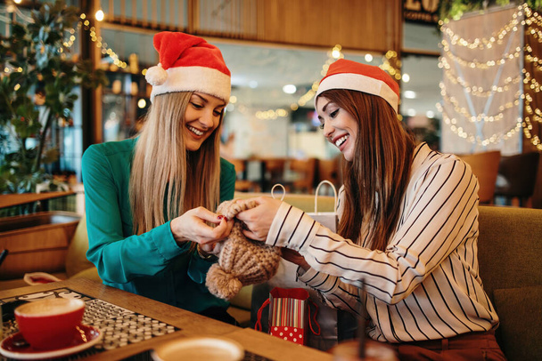 Two best friends with Santa hats sitting in coffee bar or restaurant after shopping and happily talking together. They also show each other the clothes they bought. - Photo, Image