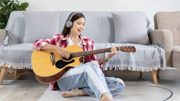 Aziatische vrouwelijke artiest die gitaar speelt en vrolijk zingt in de woonkamer, Ontspanning met muziektherapie, Vrije tijd doorbrengen met muziek, Muziekvreugde, Akoestische gitaar. - Foto, afbeelding
