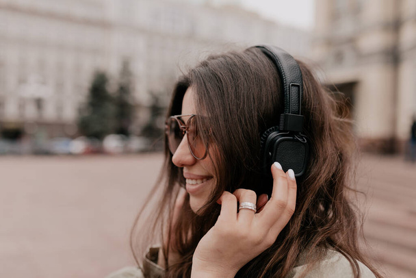 Close up profile photo of pretty cute brunette girl with happy smile, listening music and looking forward. Woman in headphone in the city  - Foto, Imagen
