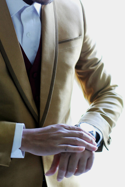 Деталі позують половину тіла чоловіка з золотим костюмом, який тримає годинник або фіксує його
. - Фото, зображення