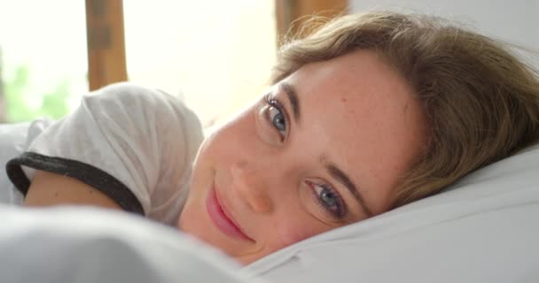 Sypialnia, obudź się i portret szczęśliwej kobiety, dzień dobry i zrelaksować się na wygodnej miękkiej poduszce w Rosji. Twarz młodej kobiety w łóżku po śnie, zdrowy odpoczynek lub drzemka dla odnowy biologicznej, spokoju i spokoju. - Materiał filmowy, wideo