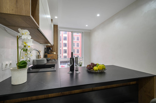 Intérieur de cuisine moderne de luxe noir et blanc, plan de travail avec fruits et vin au premier plan - Photo, image