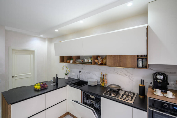 Большой черно-белый современный роскошный кухонный интерьер, вид на угол, некоторые двери мебели открыты - Фото, изображение
