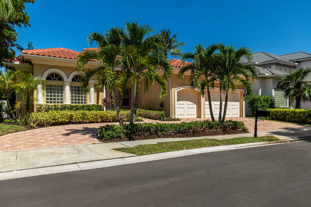 Facade of elegant colonial-style mansion in Boca Raton, with tropical front garden, cobblestone driveway, palms, trees, short grass, sidewalk, blue sky - Photo, Image