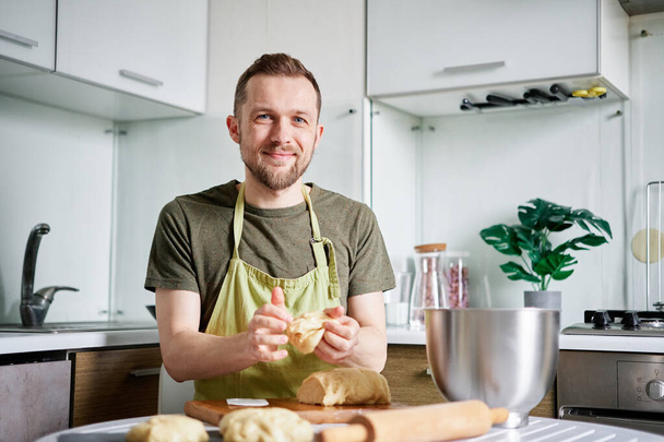Vrolijke Kaukasische chef-kok bakker in groene schort maken deeg ballen met houten snijplank op de achtergrond. Werken thuis keuken concept, zelfgemaakt bakken. Hoge kwaliteit foto - Foto, afbeelding