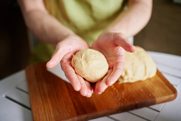 Closeup handen van de mannelijke chef-kok bakker in groene schort houden deeg bal. Werken thuis keuken concept, zelfgemaakt bakken. Onherkenbaar persoon. Hoge kwaliteit imago - Foto, afbeelding