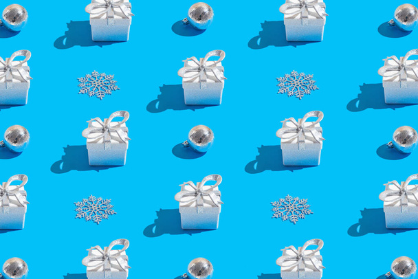 Kreatywny wzór wykonany z błyszczących białych pudełek prezentów, dekoracyjnych kulek i płatków śniegu na niebieskim tle. Boże Narodzenie lub urodziny pomysł na prezent. Temat wakacji. Minimalny styl. - Zdjęcie, obraz