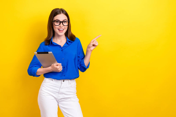 Photo of young assistant lady wear blue shirt brunette hair finger direct empty space hold apple ipad sale isolated on yellow color background. - Fotó, kép