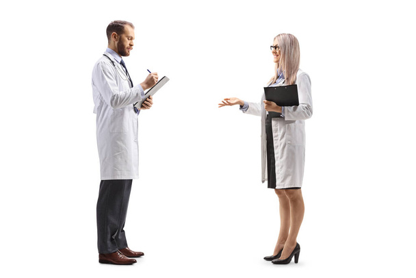 Full length profile shot of a male and female doctor standing and discussing isolated on white background  - Photo, image