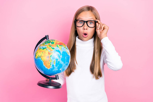 Portrait of impressed smart girl hold globe arm touch eyeglasses open mouth isolated on pink color background. - Foto, afbeelding