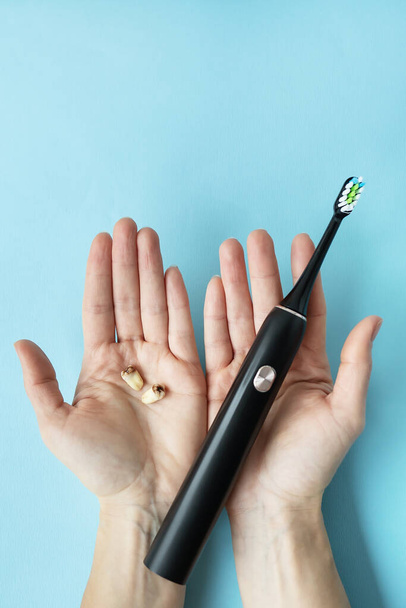 A modern electric toothbrush in one hand and pulled teeth in the other hand on a blue background. Tooth extraction operation. The concept of hygiene for daily care of the oral cavity in order not to lose a tooth - Photo, Image